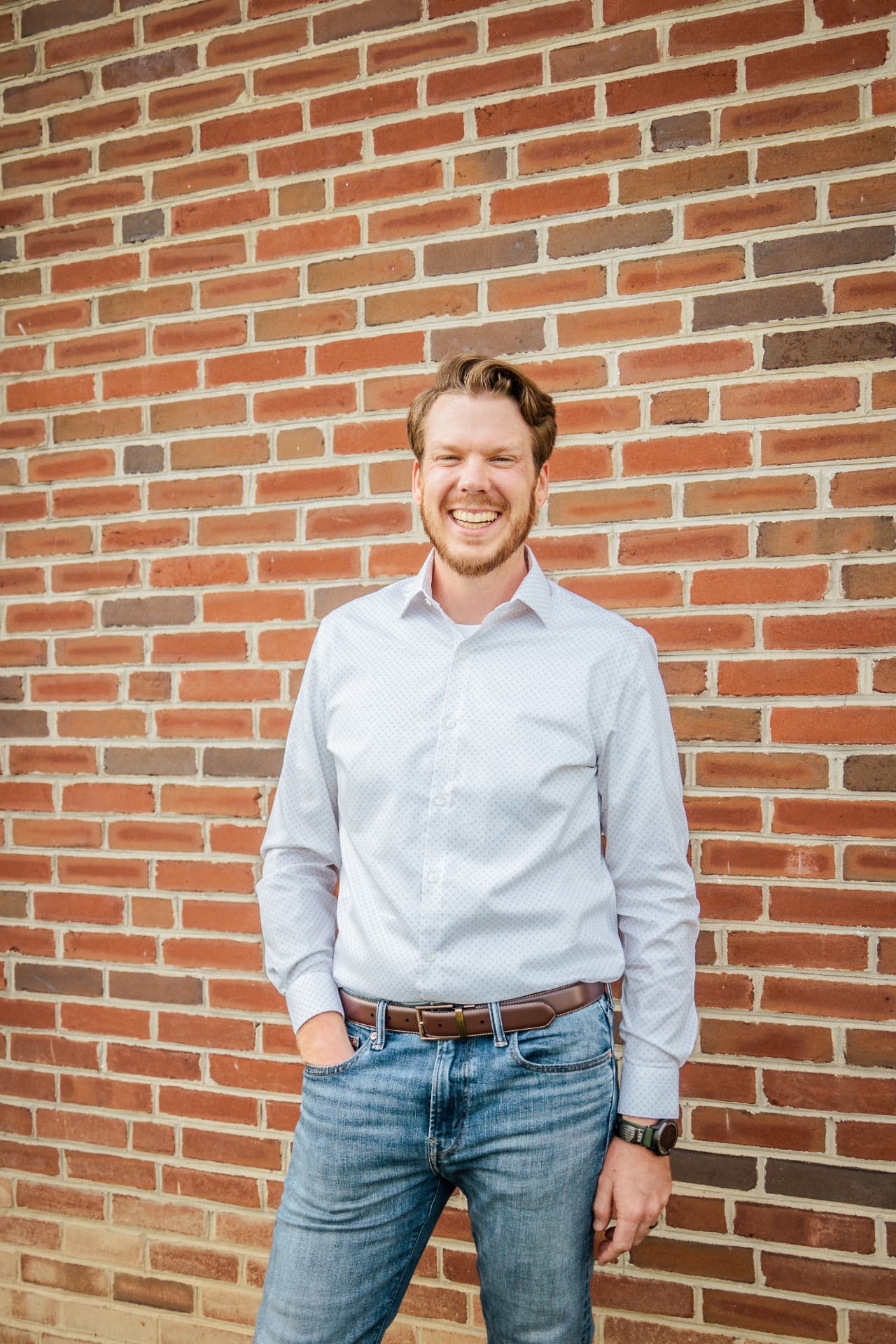 Portrait of Brice, founder of Verus Ridge Digital, smiling in a light button-down shirt against a brick wall