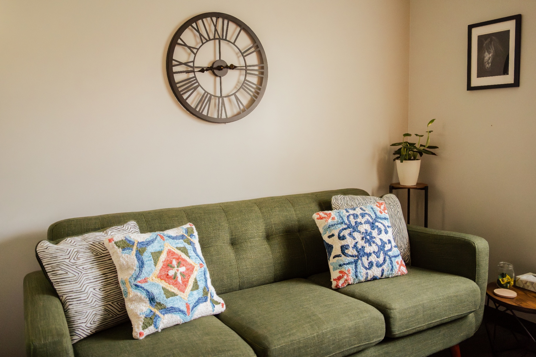 Green mid-century sofa with patterned pillows beneath a large wall clock in a therapy office